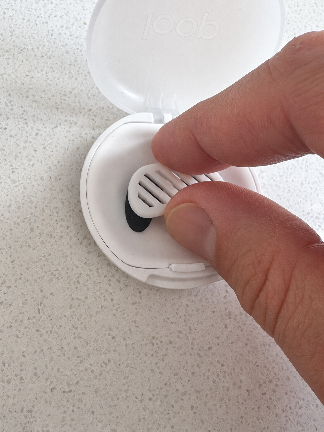 Fingers lifting a slotted wearable prototype from an open white case